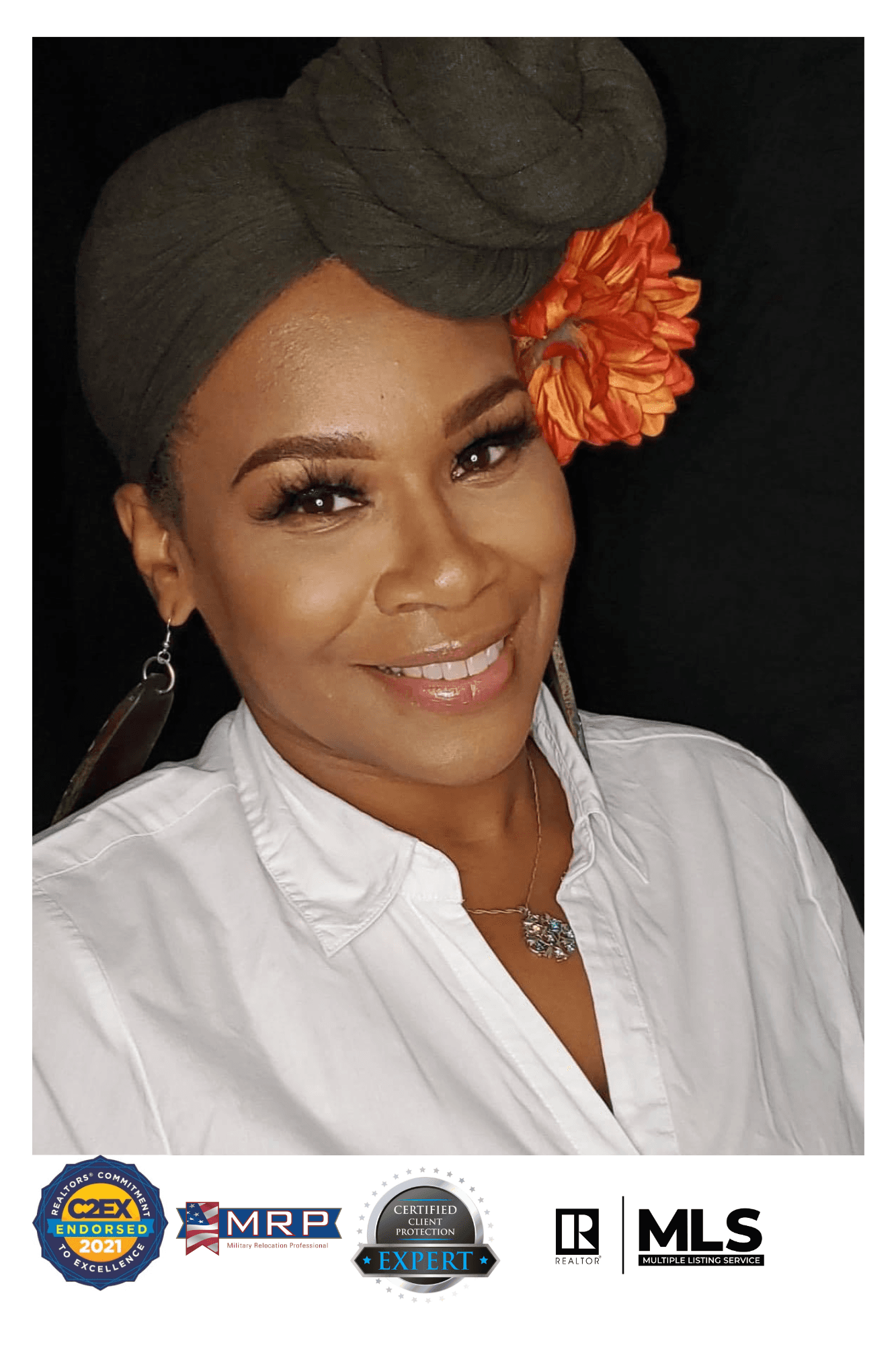 Smiling woman wearing a grey headwrap with an orange flower accessory and white collared shirt.